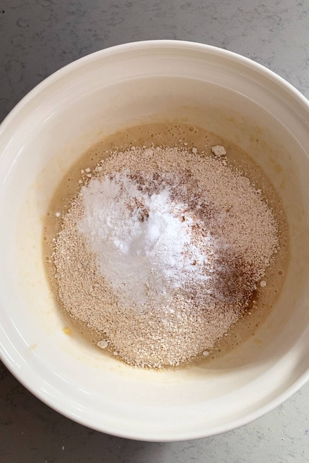 Dry ingredients sitting on top of a wet batter in a mixing bowl before stirring.