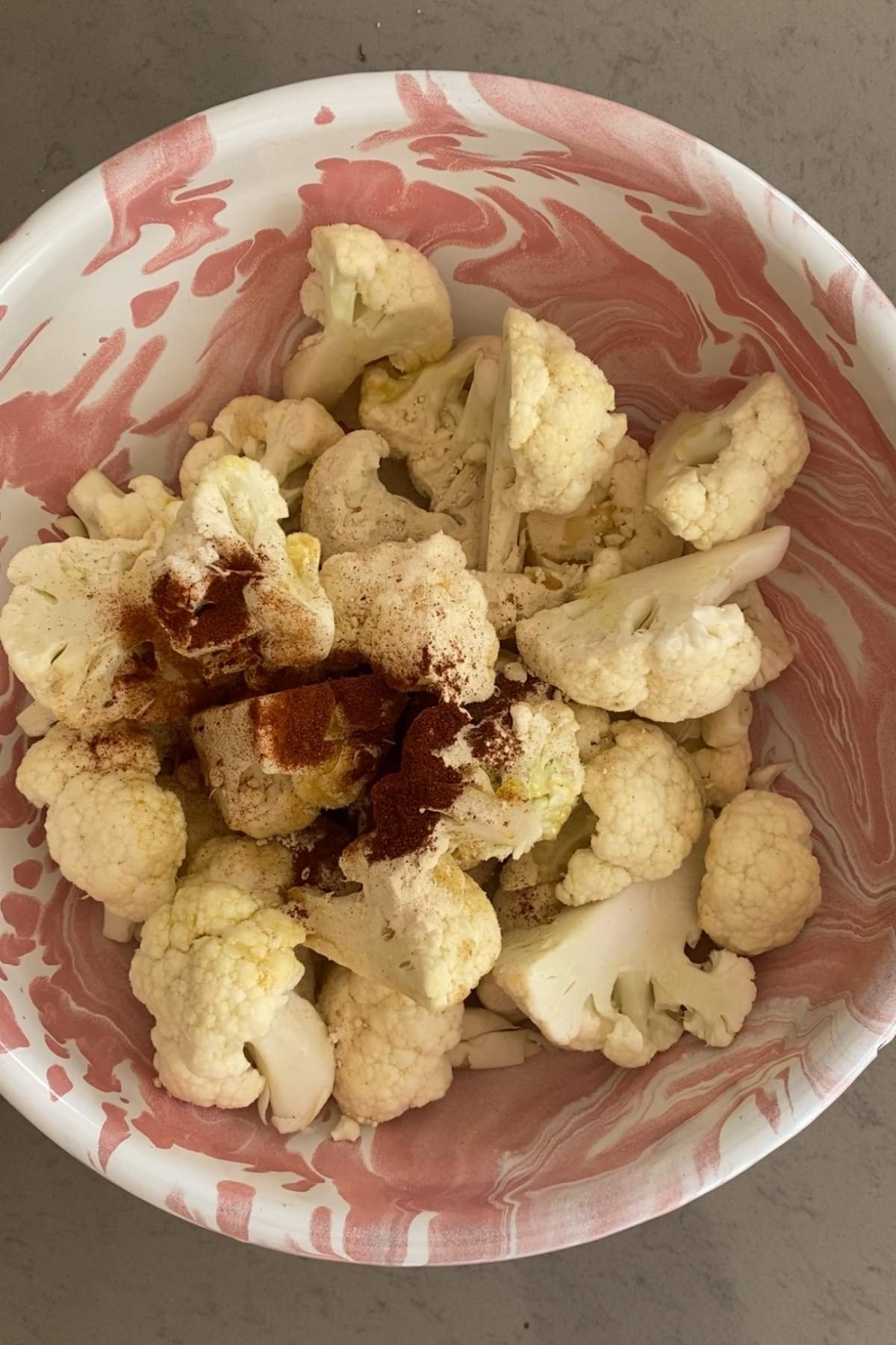 Raw cauliflower florets in a bowl sprinkled with visible dry spices.