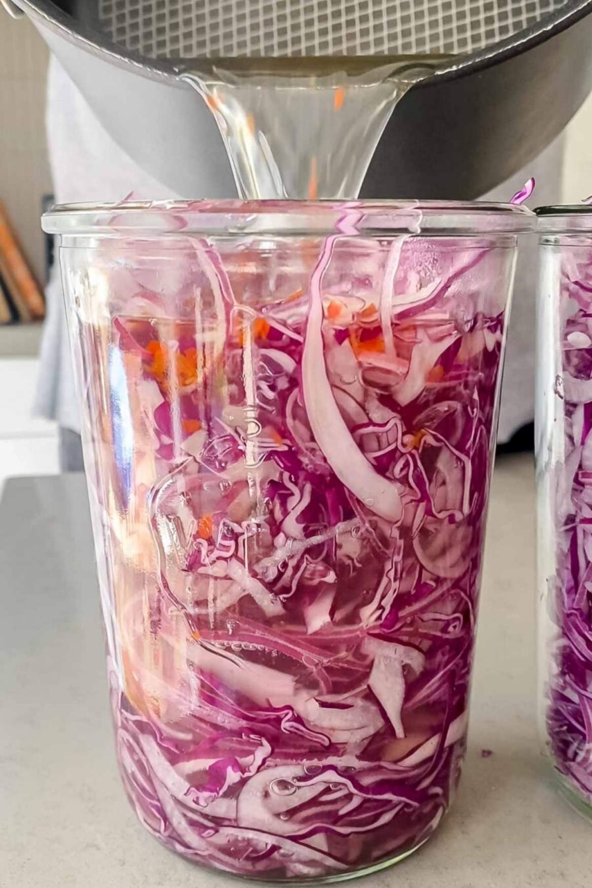Hot liquid being poured into a jar packed with shredded purple cabbage.
