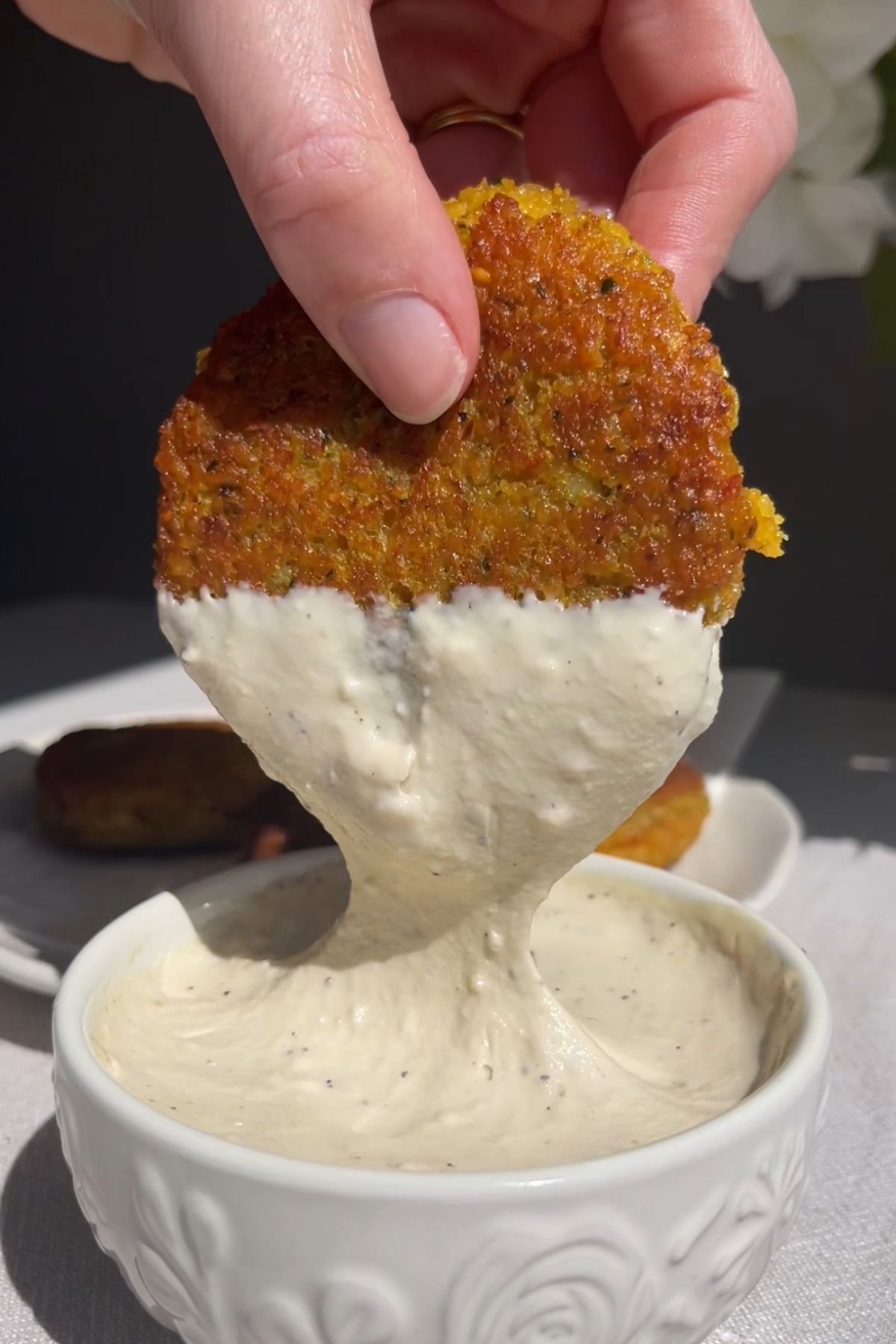 A hand dips a golden fritter into a thick creamy white sauce.