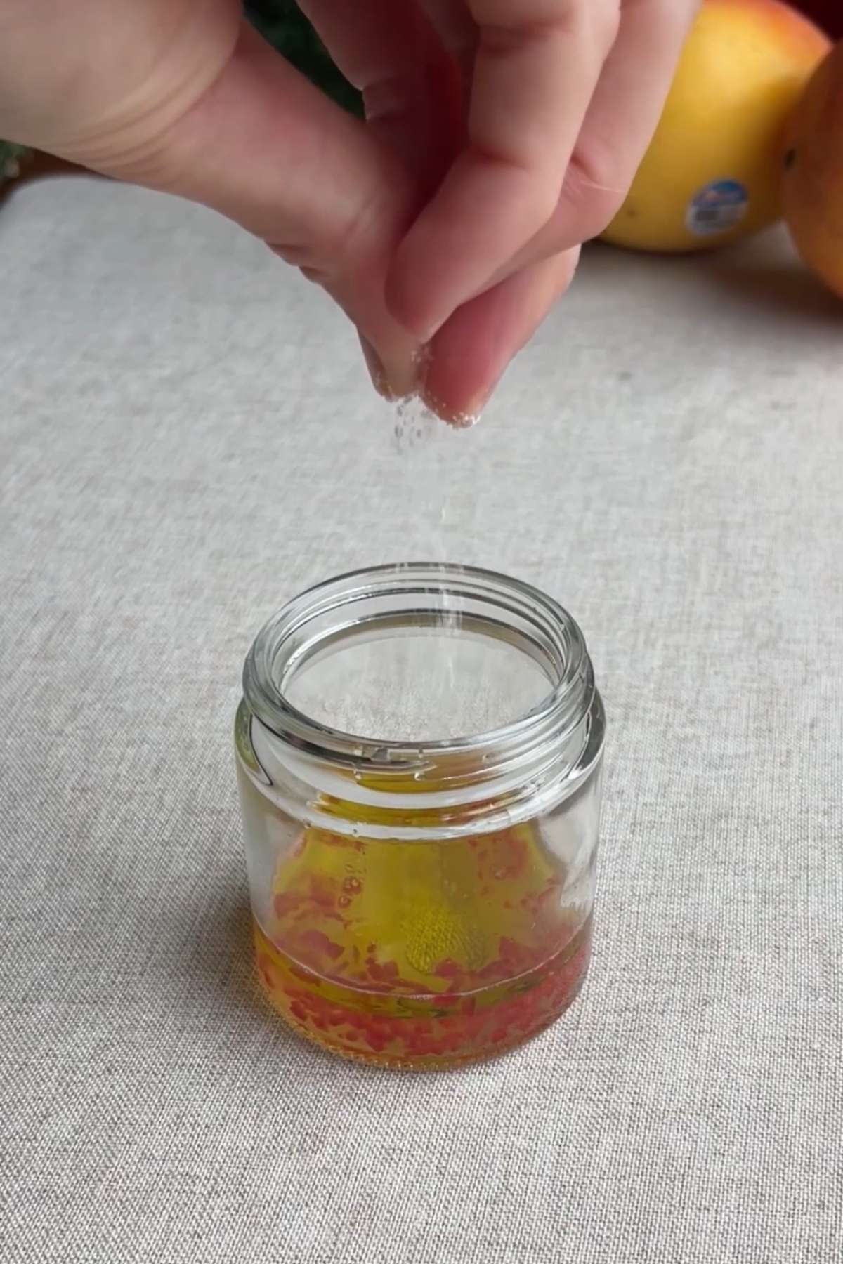 Hand sprinkling salt into a small jar of olive oil, lime juice, and chopped red chili.