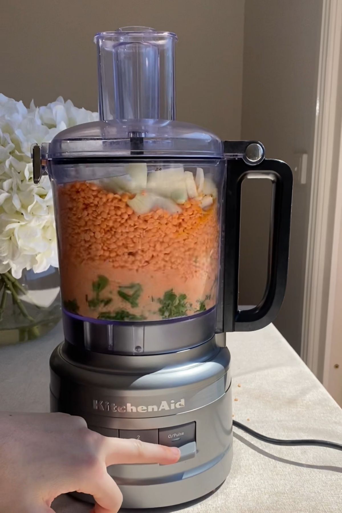A food processor filled with red lentils, onion pieces, and fresh herbs before blending.