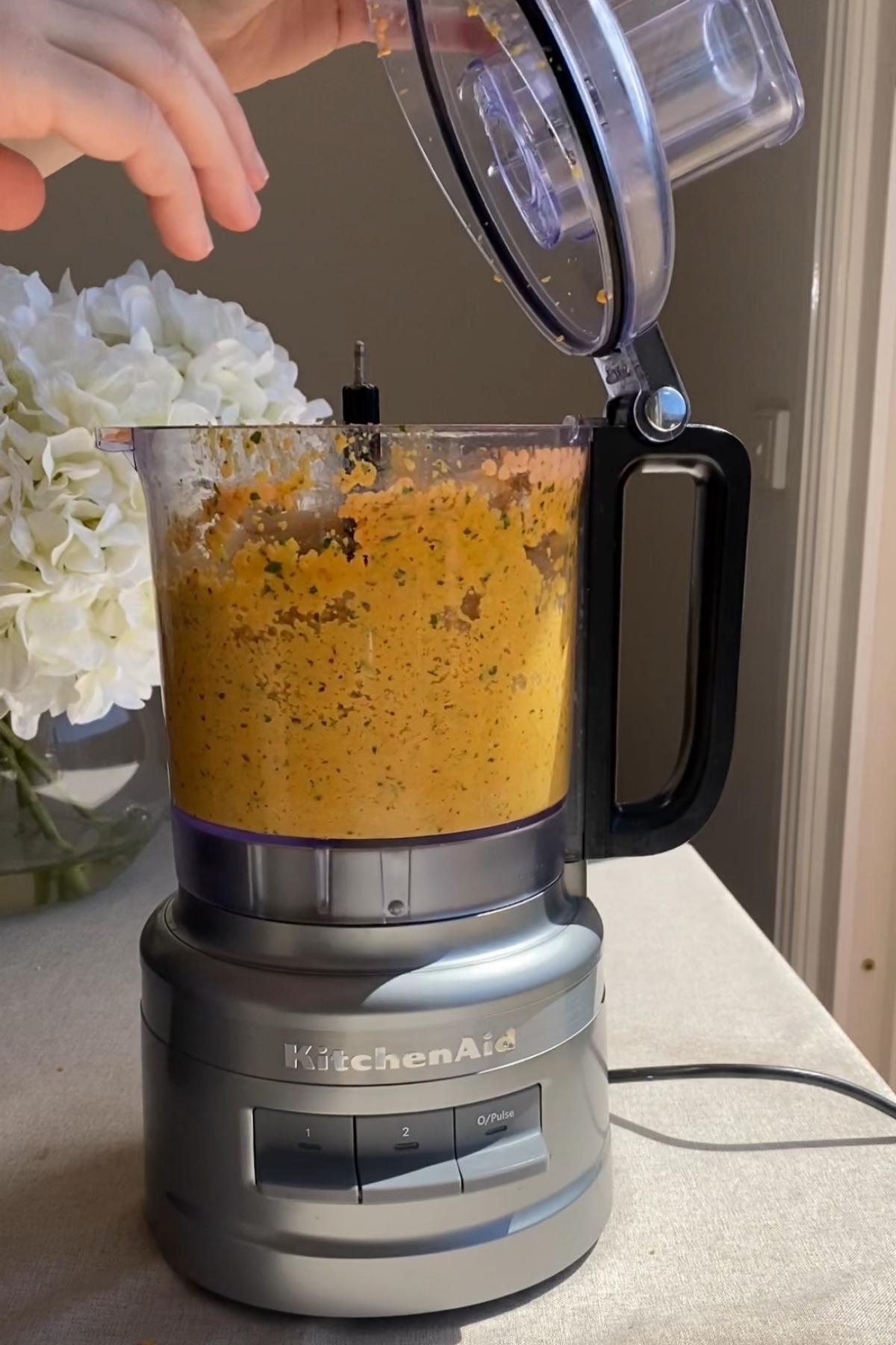 Blended lentil mixture with herbs inside a food processor, lid being lifted.