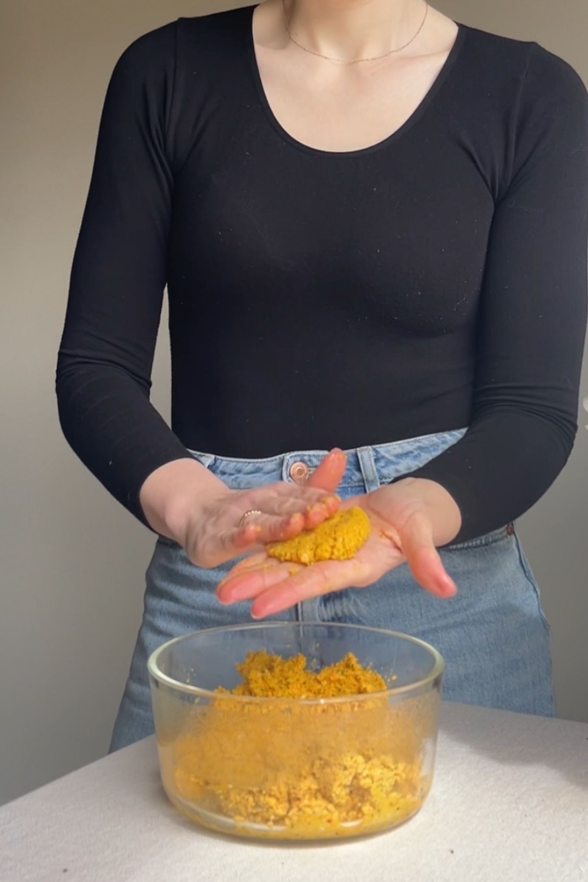 Person in black top shaping orange lentil mixture into patties over a glass bowl.