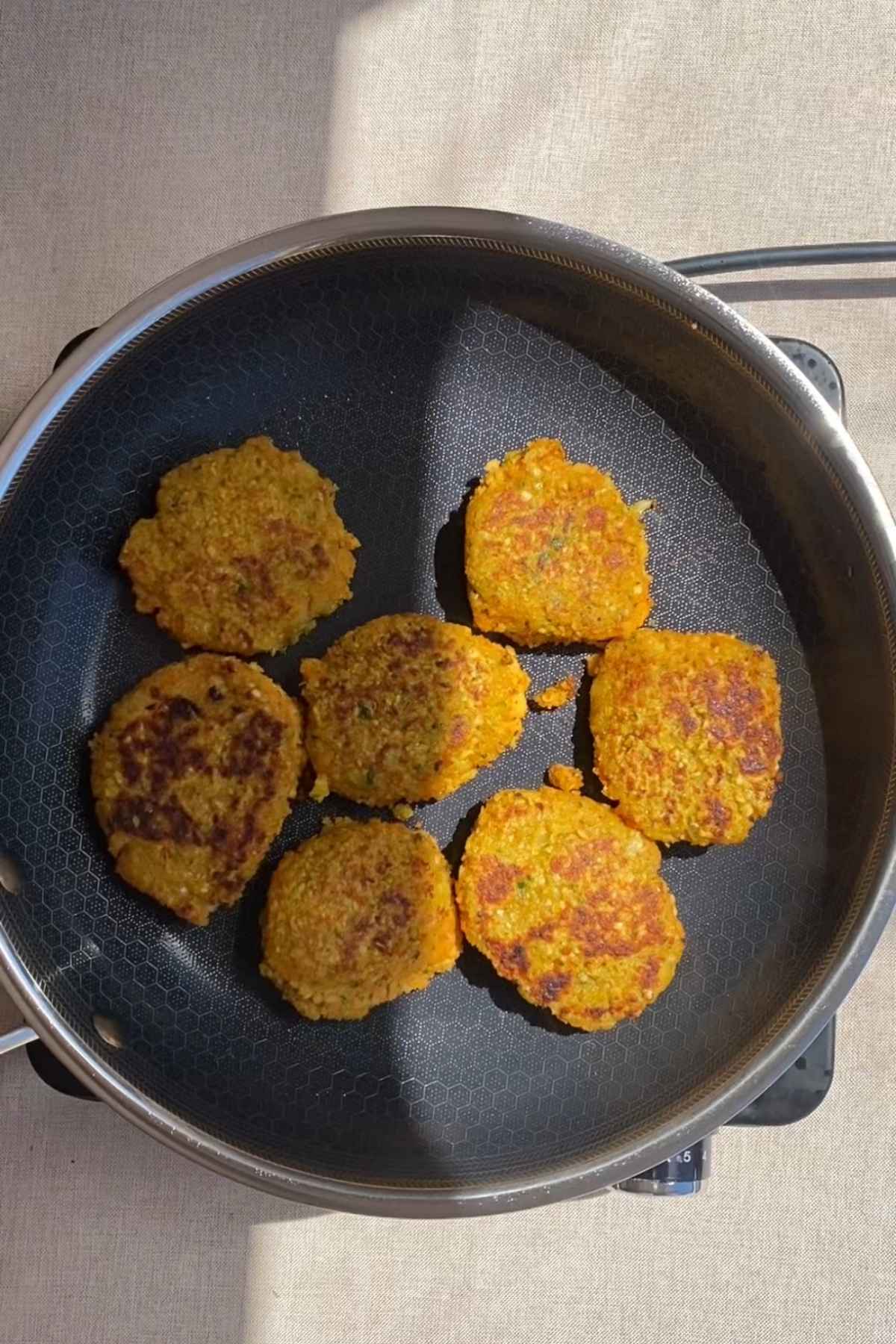 Golden lentil fritters cooking in a pan, crisp and lightly browned on top.