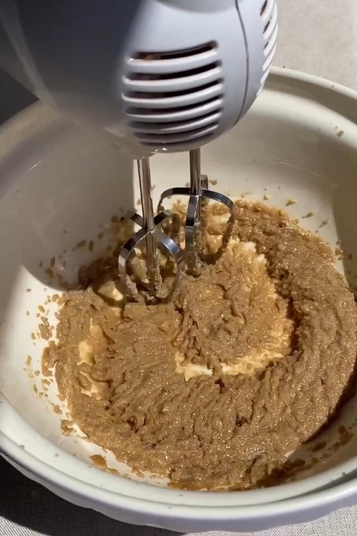 Electric beaters creaming butter and sugar into a smooth mixture in a bowl.