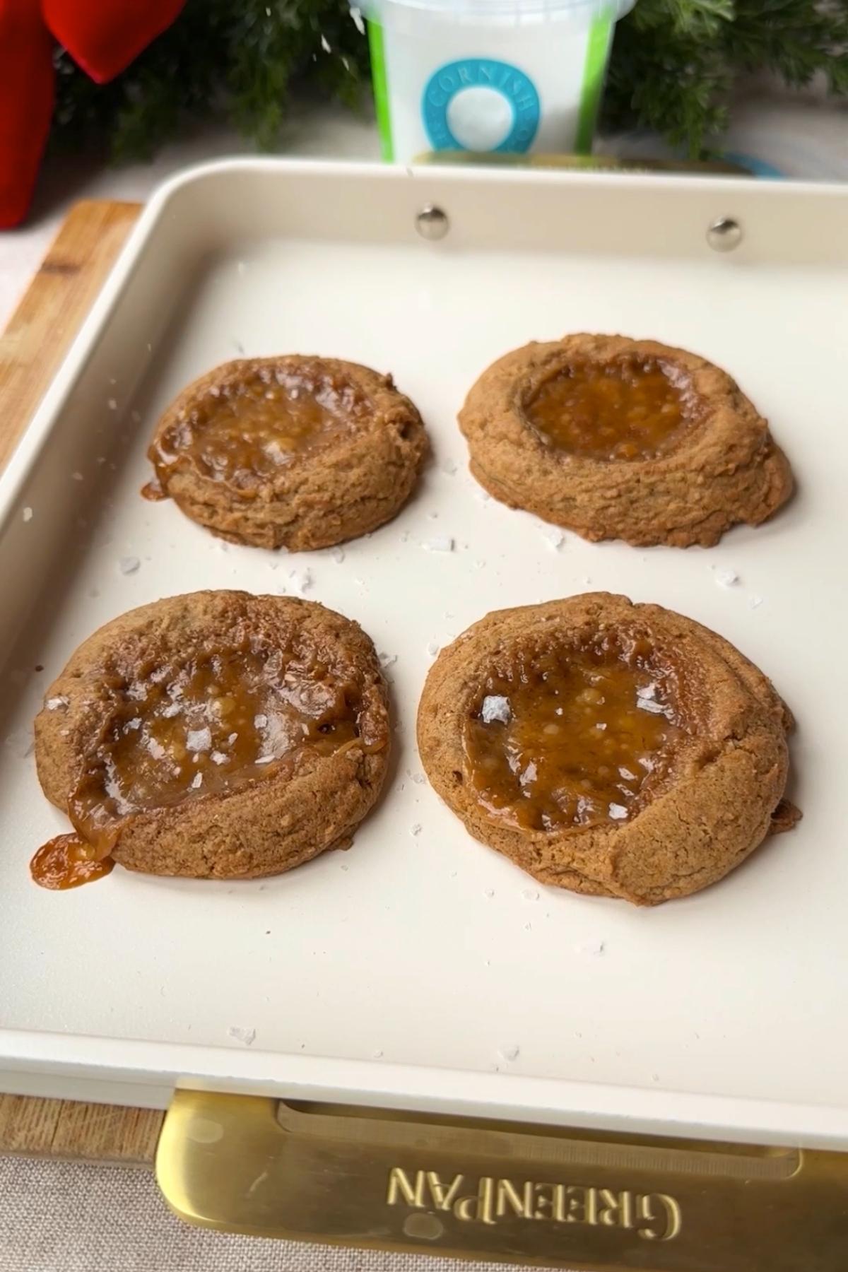 Soft caramel-filled cookies cooling on a baking tray with a light sprinkle of sea salt.