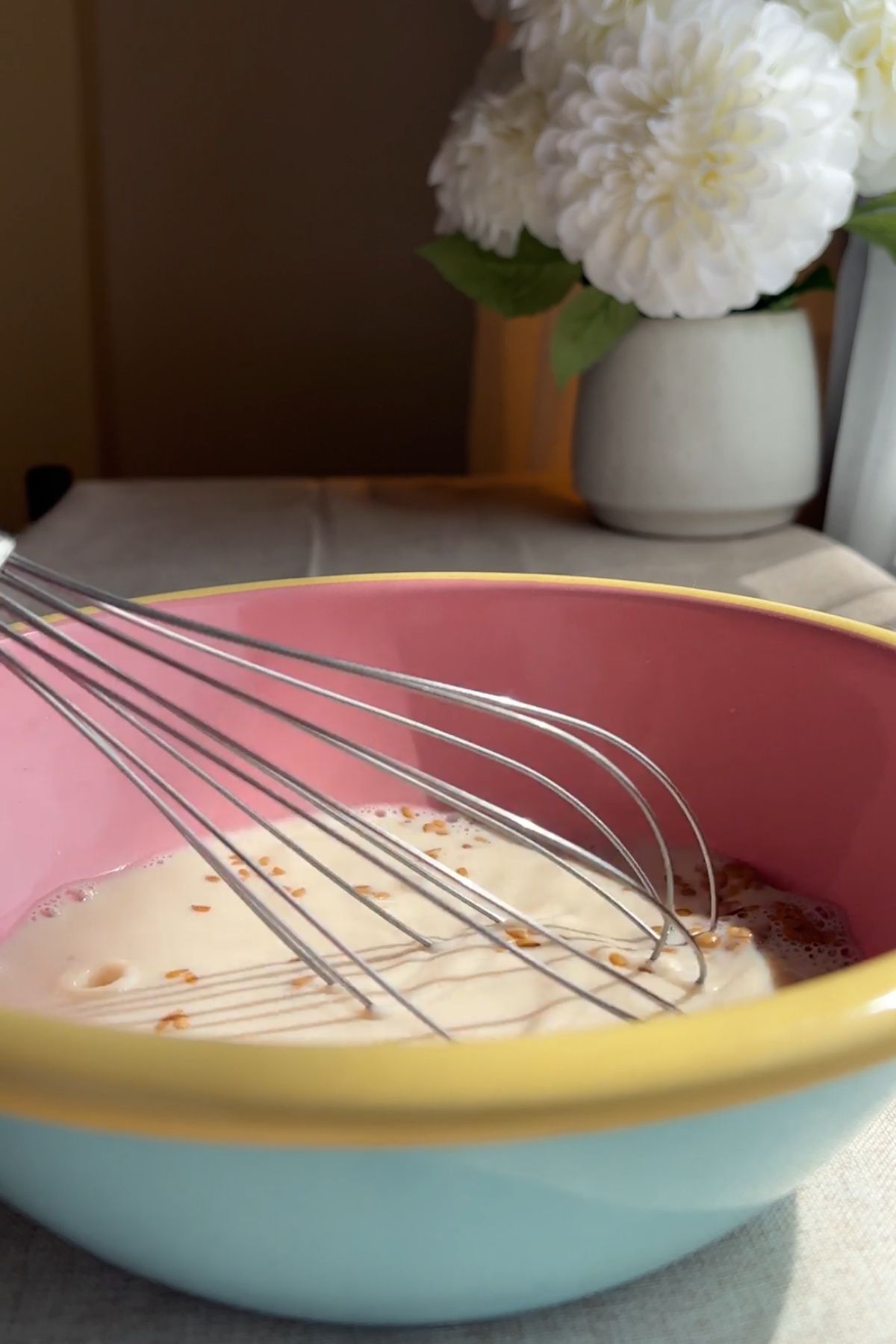 A whisk resting in a bowl of wet ingredients with small flax specks.