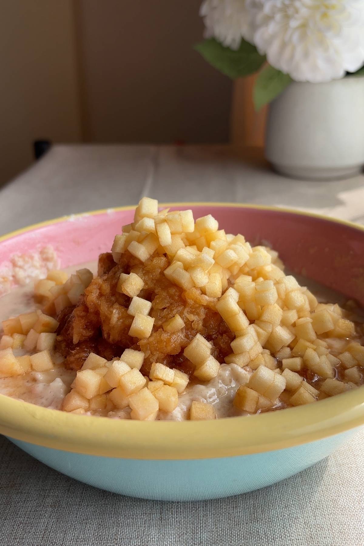 Cooked oats topped with finely diced apple in a pink and yellow bowl.