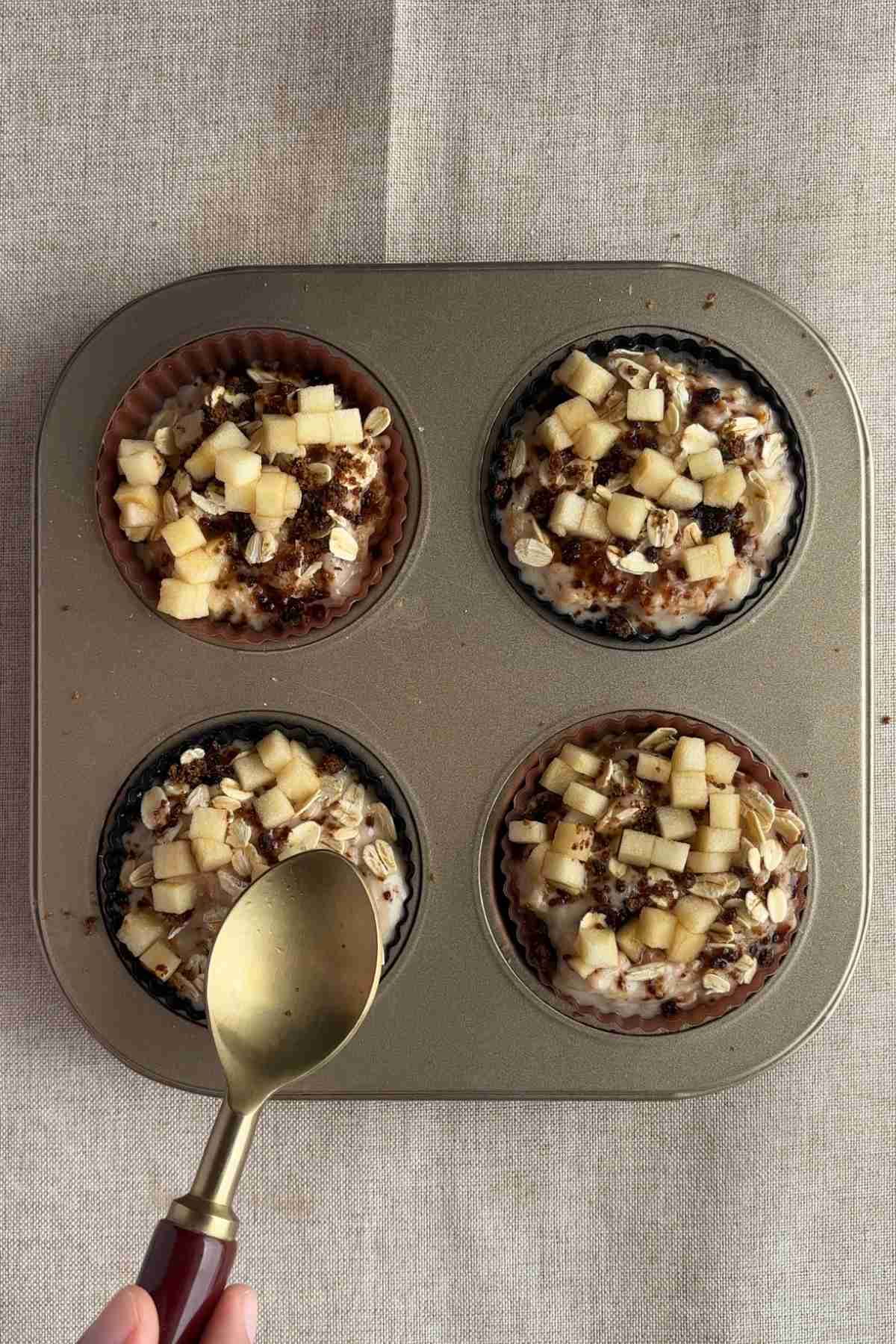 Muffin batter in silicone cups topped with diced apple and oats in a muffin tray.