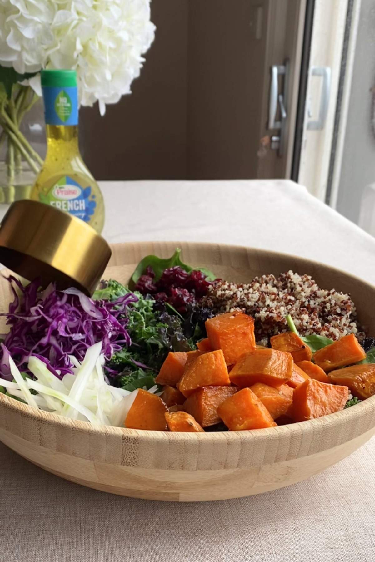 Wooden bowl filled with kale, quinoa, roasted sweet potato, and cabbage.