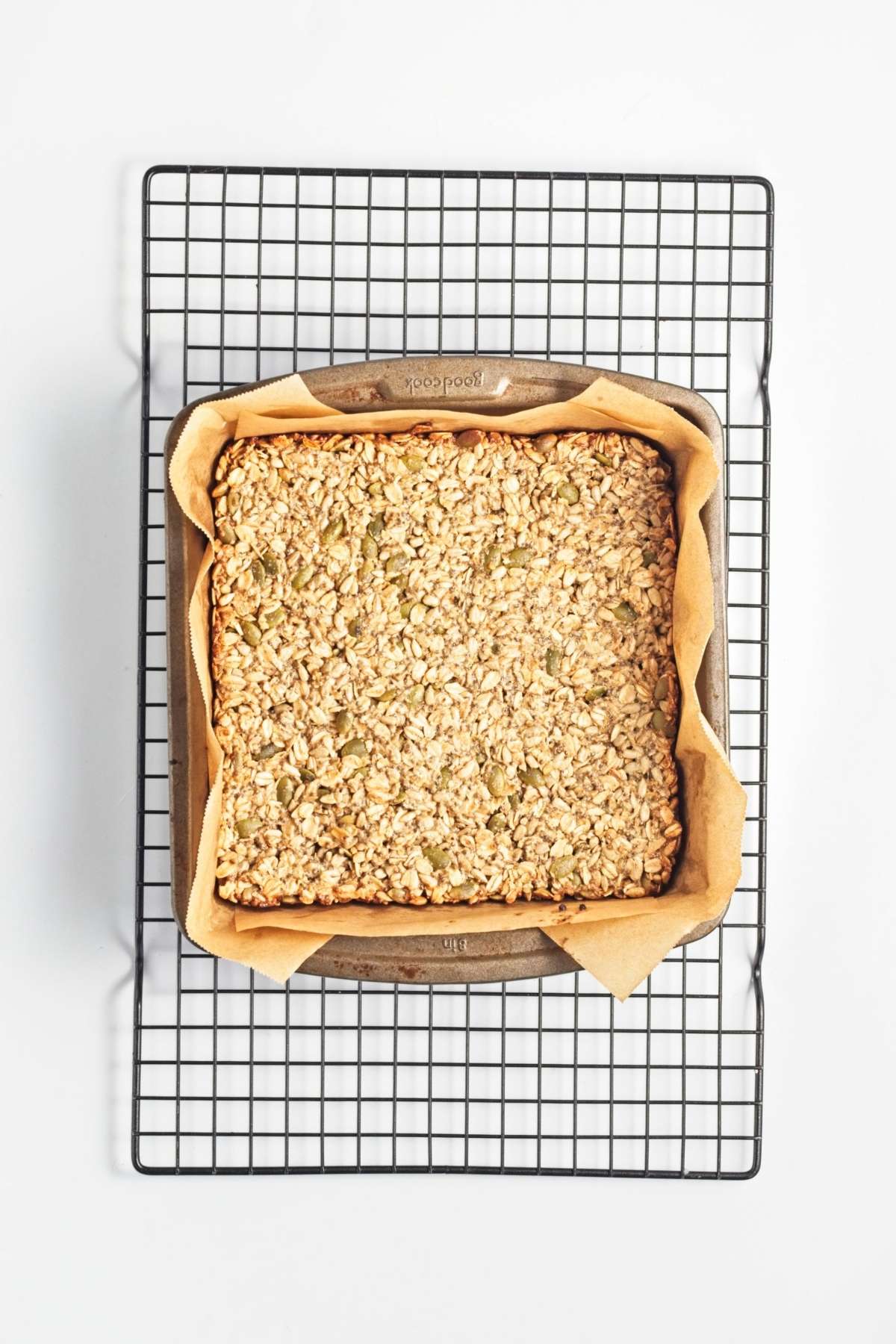 Golden baked oat-and-seed bars cooling in a parchment-lined pan on a wire rack.