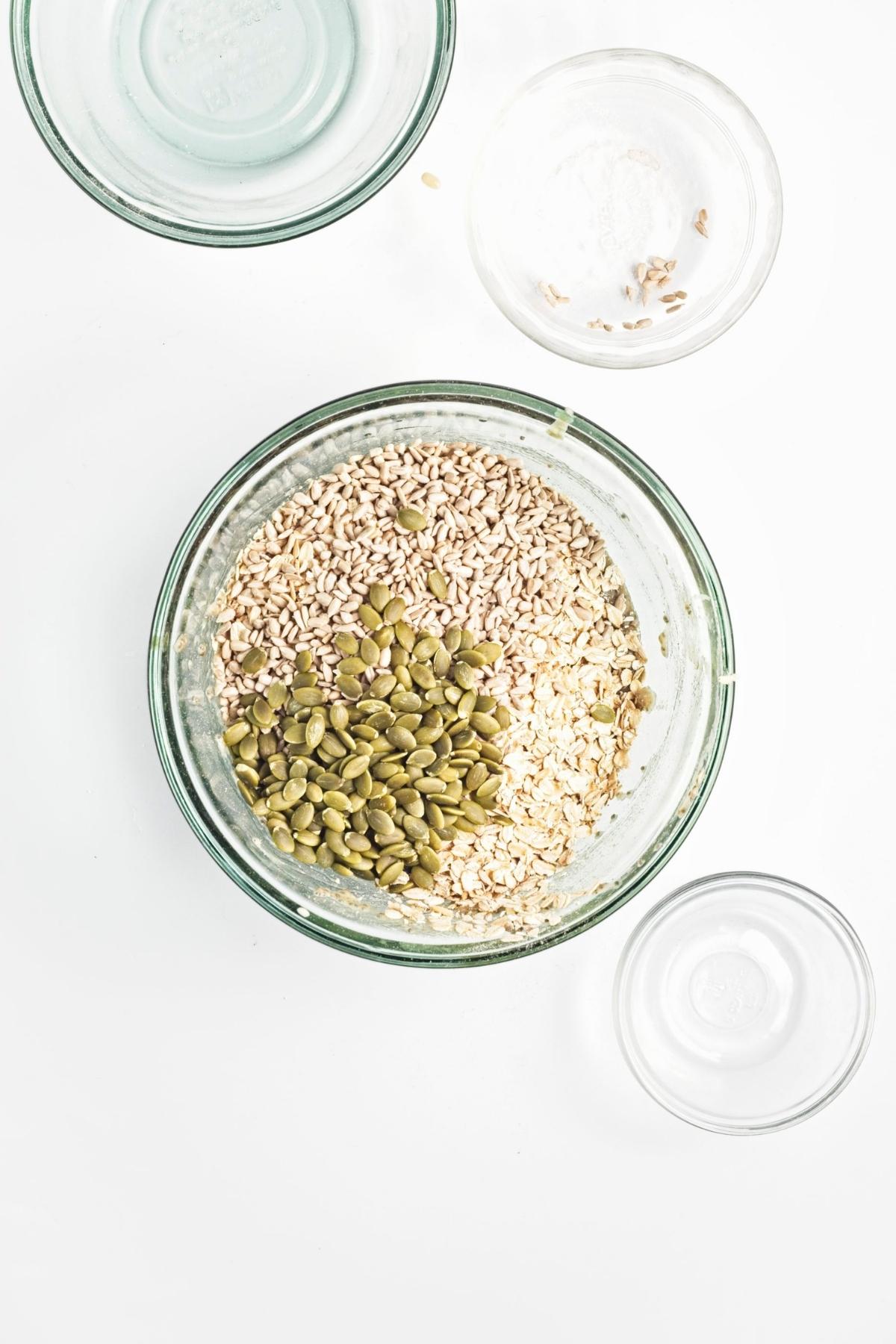 Rolled oats, sunflower seeds, and pumpkin seeds added to the wet mixture in a bowl.