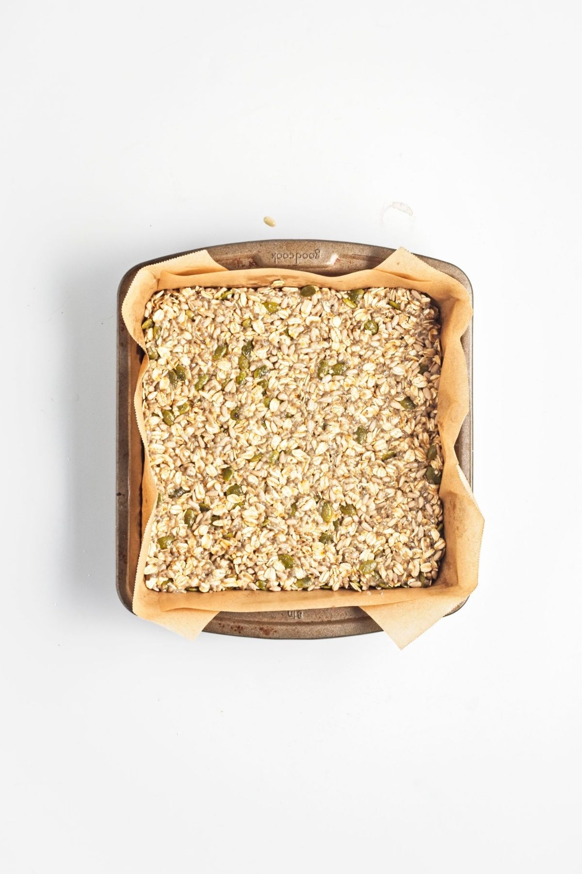 Granola bar mixture pressed firmly into a parchment-lined square baking pan.