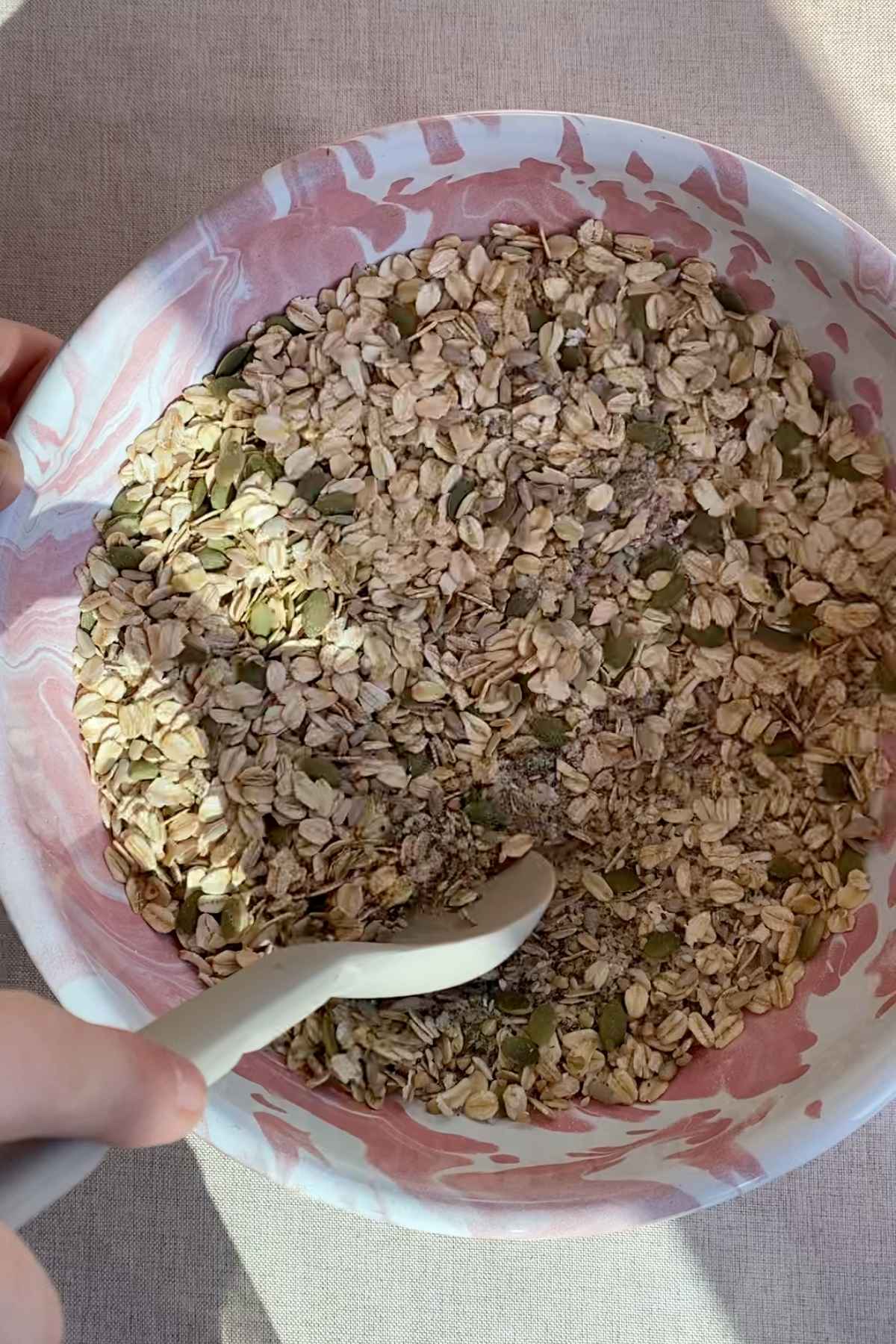Dry mix of oats, seeds, and grains in a pink marbled bowl with a spoon.