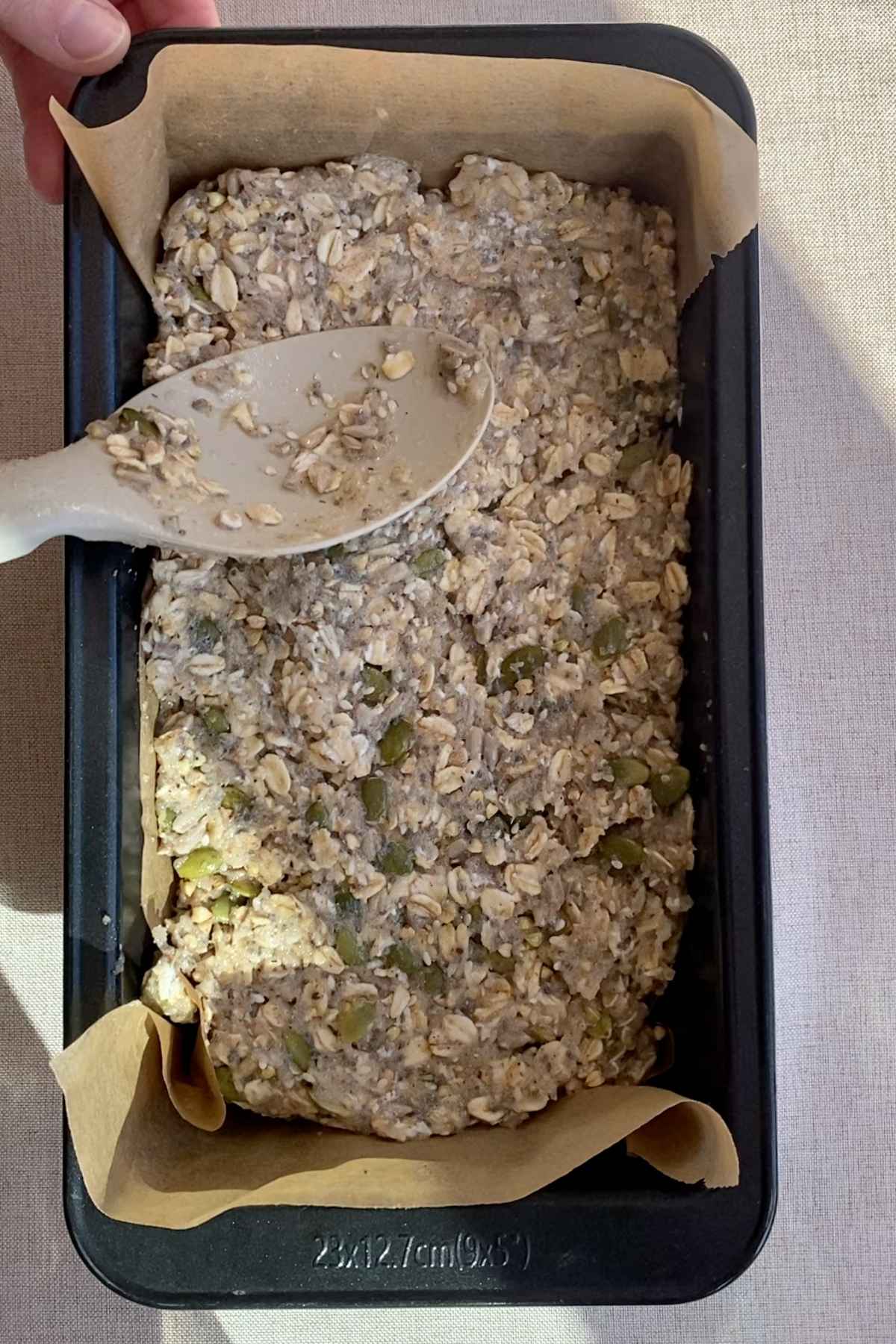 Seeded oat mixture pressed firmly into a parchment-lined loaf pan.