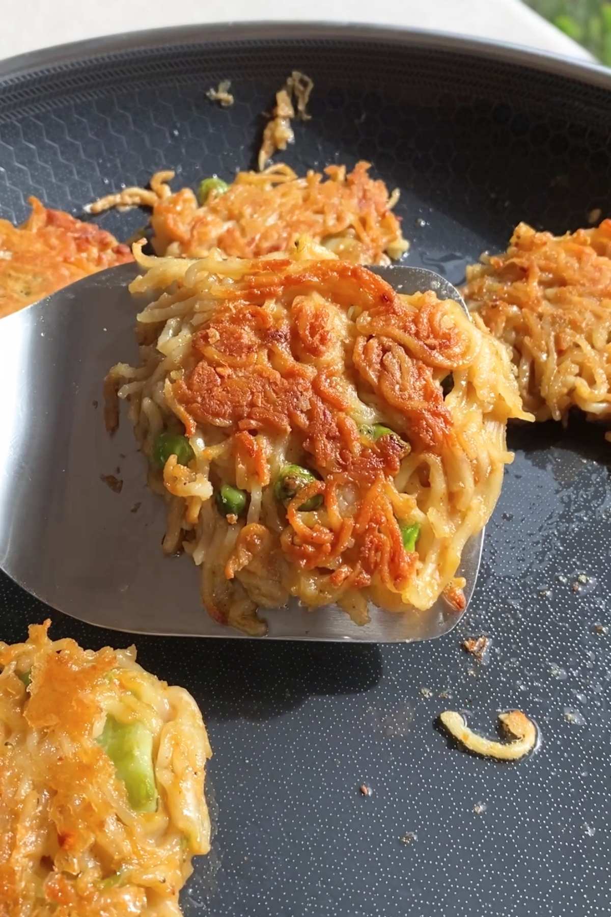 Crispy noodle patty lifted from frying pan.