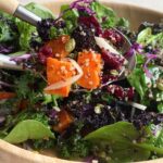 Spoons mixing salad with kale, quinoa, sweet potato, and cabbage.