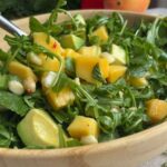 Fresh arugula salad with chunks of mango and avocado in a wooden bowl.