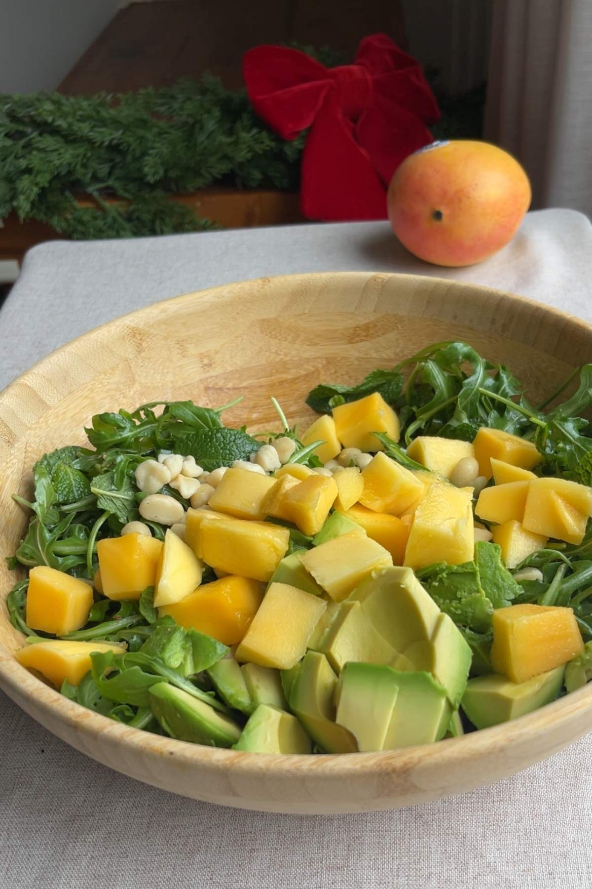 Wooden bowl filled with arugula topped with diced mango, avocado and macadamias.