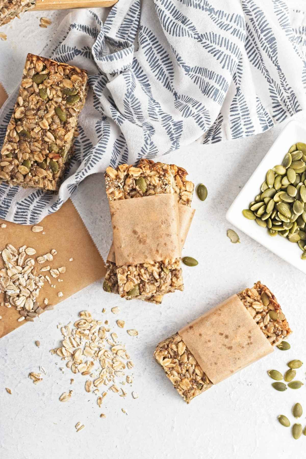 Stacked granola bars wrapped in parchment, surrounded by loose oats and seeds.