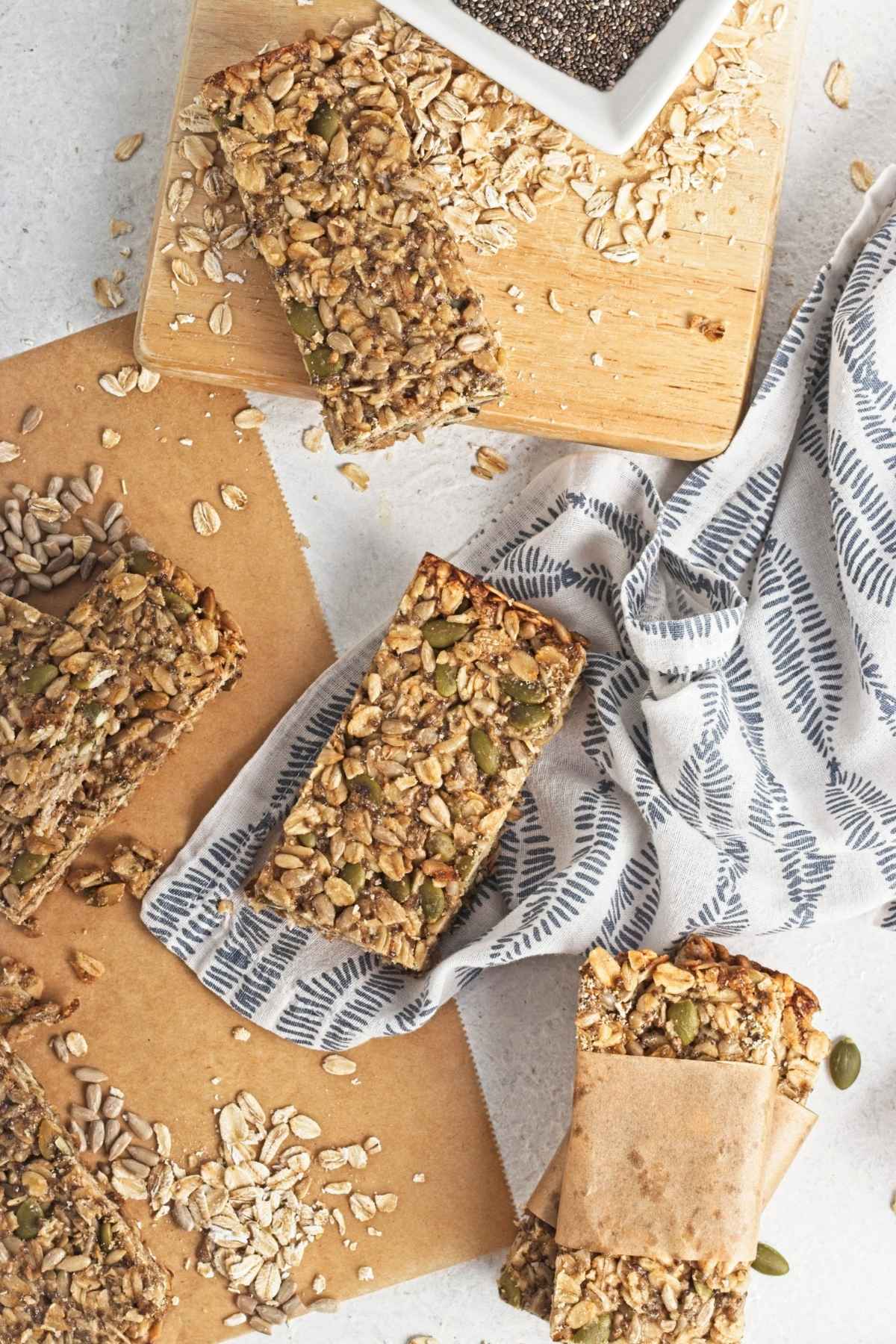 Overhead of oat and seed granola bars with scattered oats on parchment and a patterned cloth.