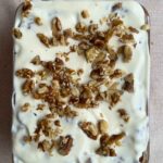 Frosted baked oats topped with chopped walnuts in a glass dish.