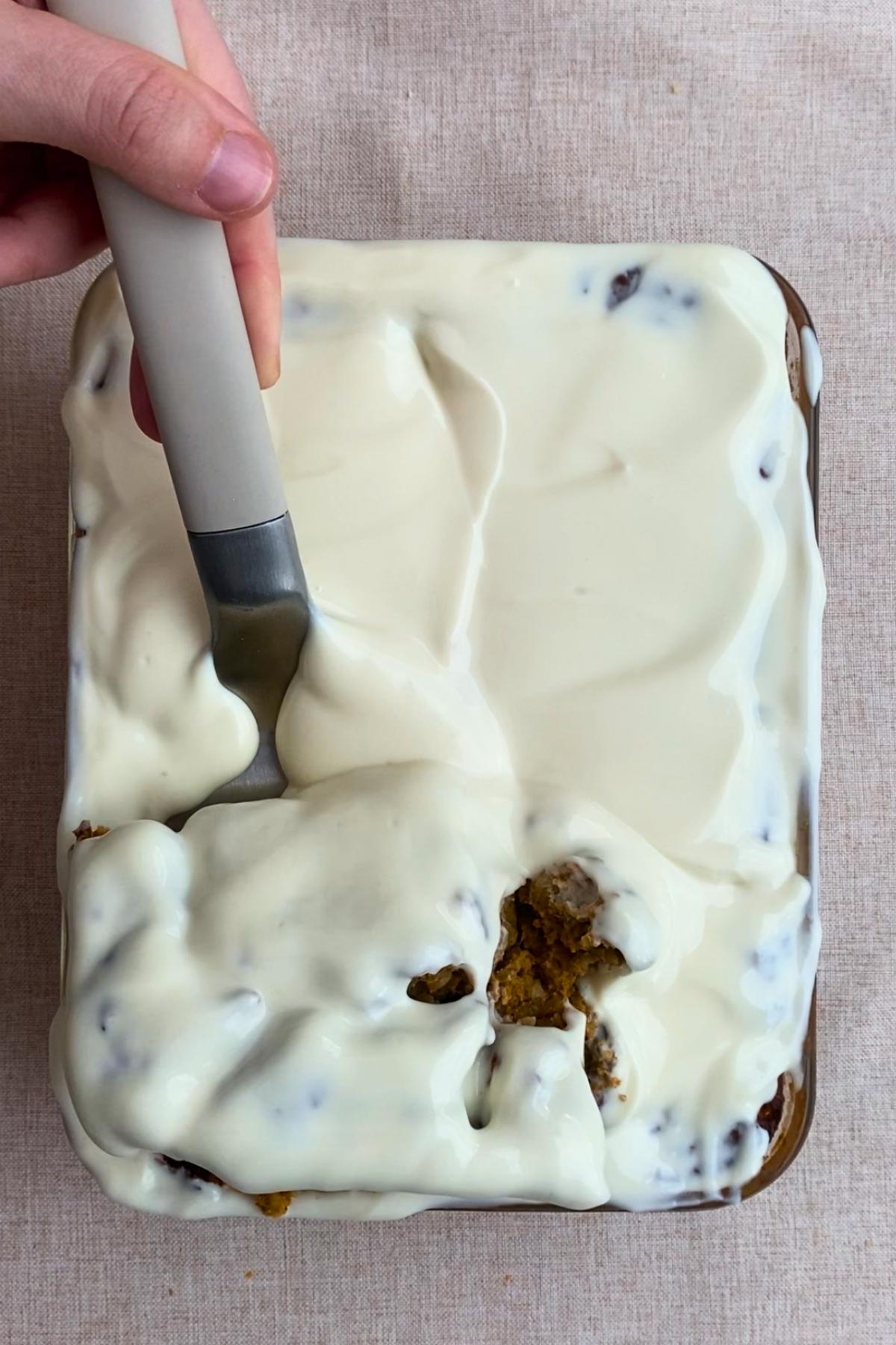 Cutting into a frosted baked oat slice with a spatula, revealing the soft pumpkin-colored center.