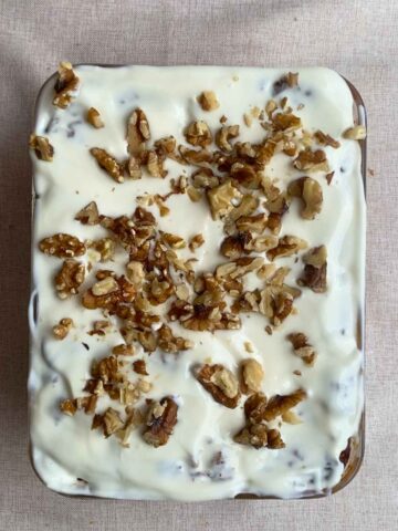 Frosted baked oats topped with chopped walnuts in a glass dish.