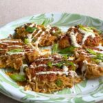 Noodle patties topped with creamy sauce, sesame seeds, and green onions on a plate.