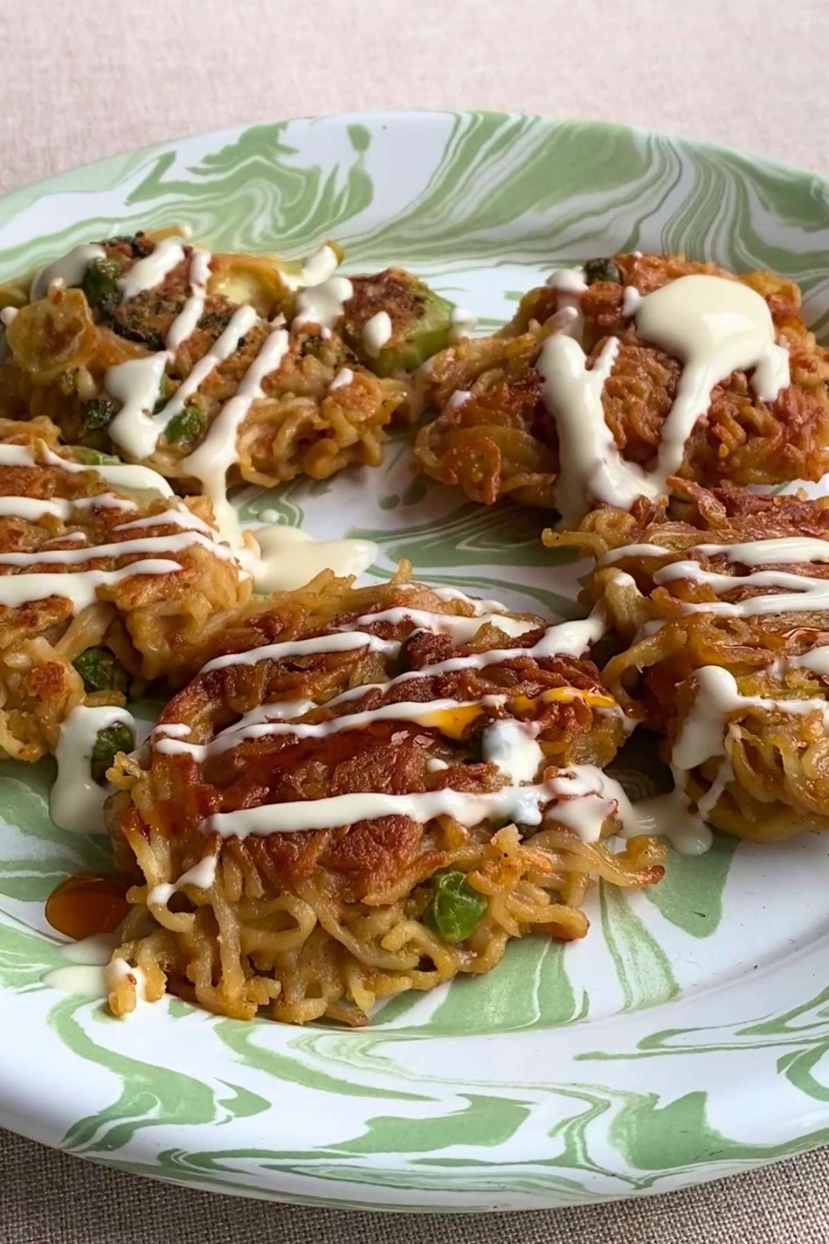 Plate of crispy noodle patties drizzled with creamy sauce.