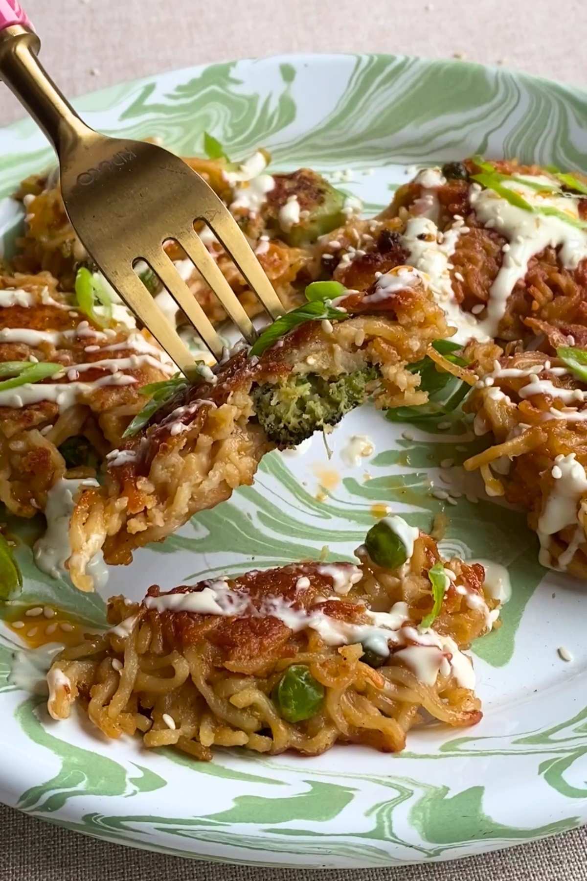 Fork cutting into a noodle patty with broccoli inside.