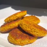 Stack of golden brown lentil fritters on a white plate in sunlight.