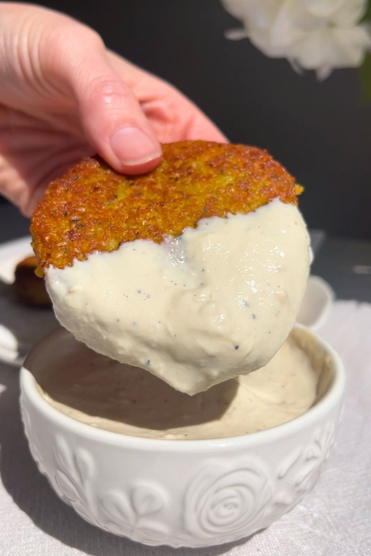 Hand dipping a golden fritter into thick creamy white sauce.