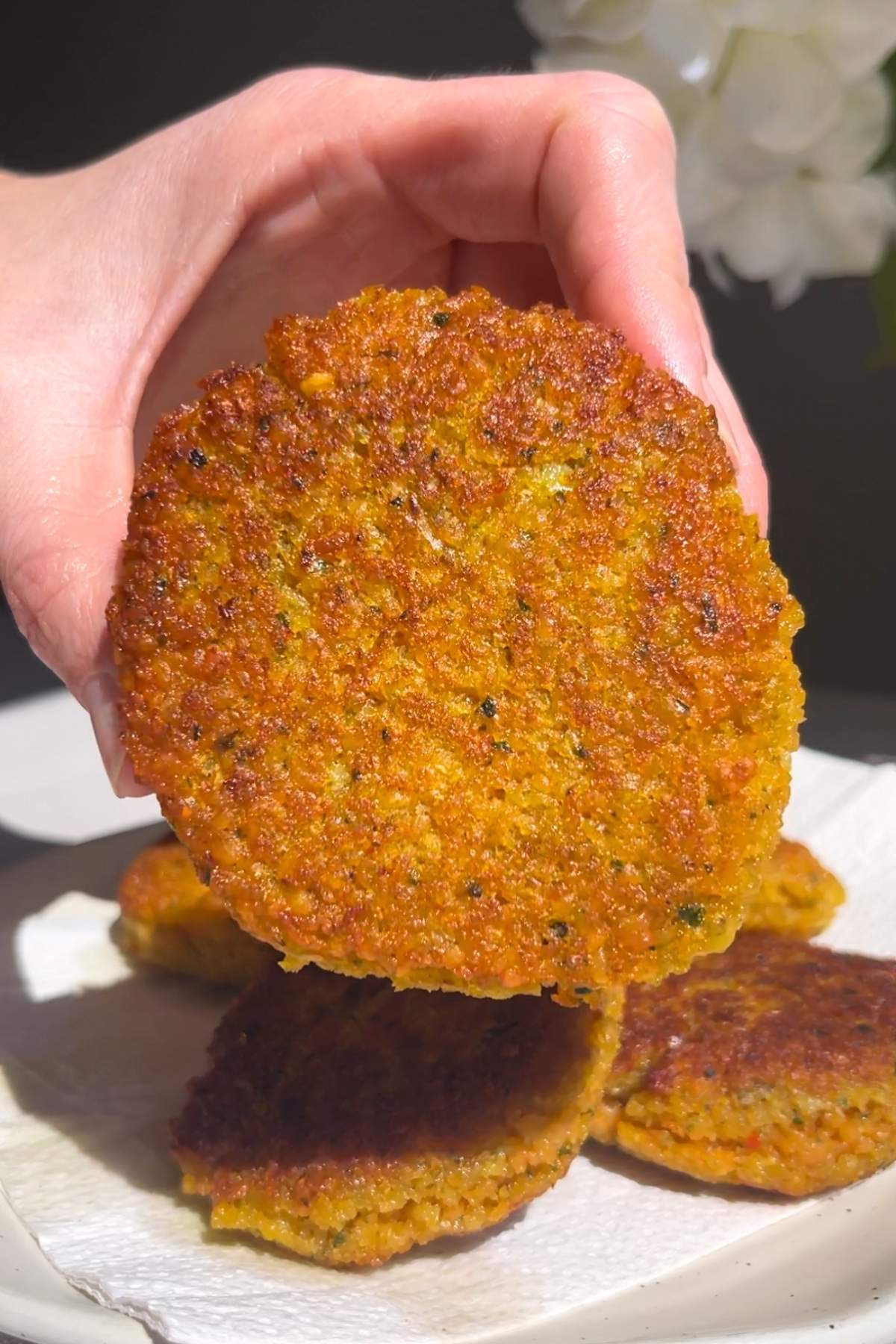 Hand holding a crisp golden lentil fritter above a plate.