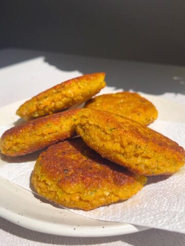 Stack of golden brown lentil fritters on a white plate in sunlight.