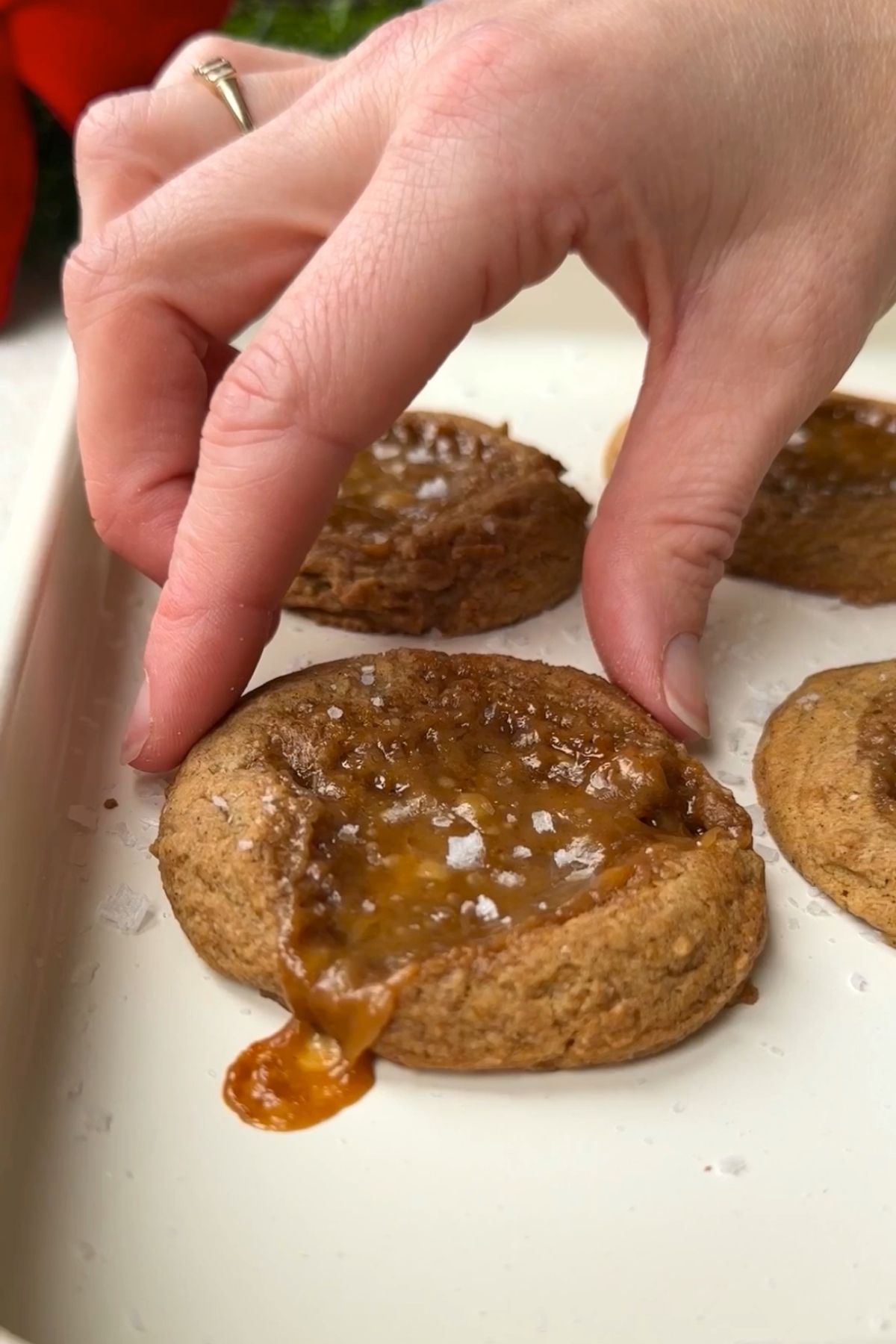 Hand lifting a soft caramel-filled cookie from a baking tray.