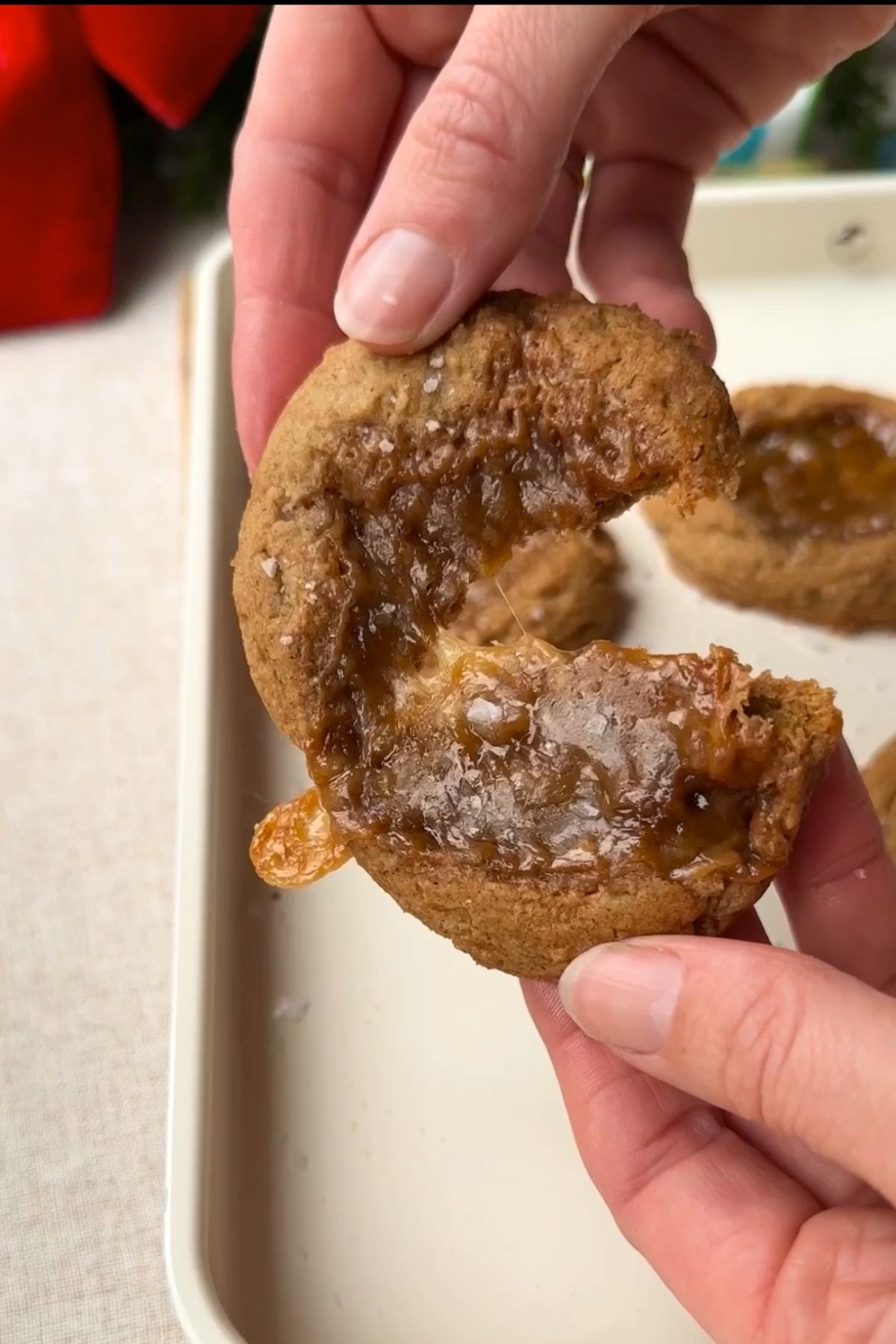 Hands holding a warm caramel-filled cookie, showing a gooey centre after a bite.