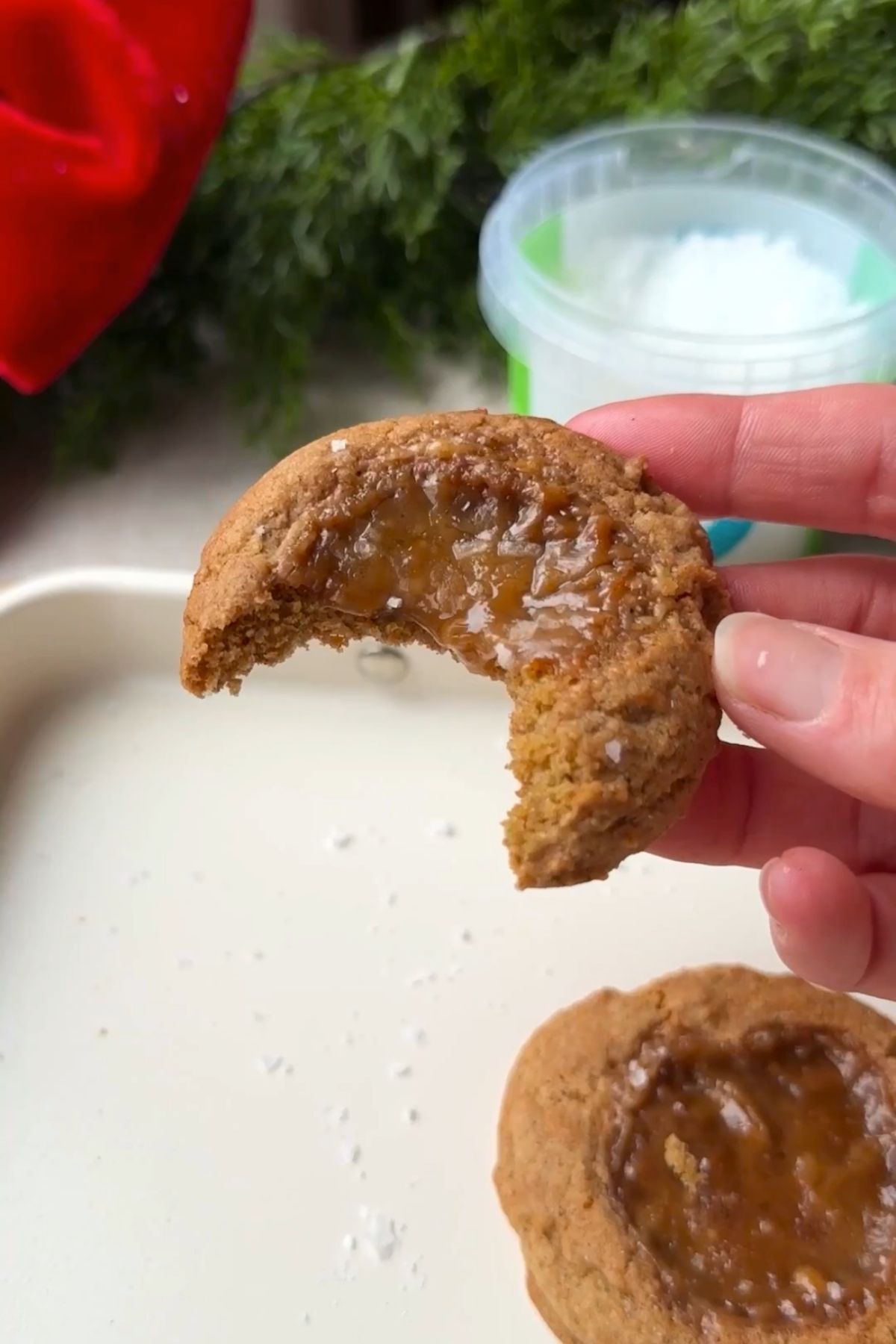 Caramel-filled cookie with a bite taken out, held up above the tray.