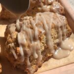 Close-up of glaze being poured from a spoon onto a warm scone.