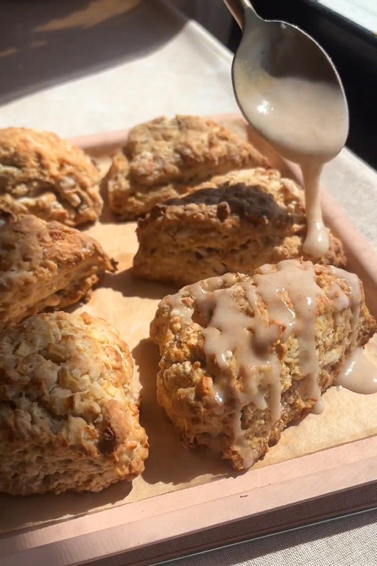 Spoon hovering above scones as glaze is drizzled over the top.