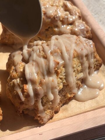 Close-up of glaze being poured from a spoon onto a warm scone.