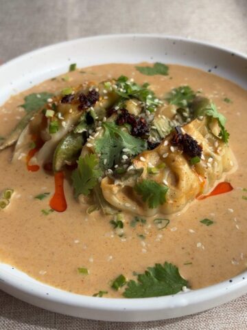 Close-up of baked dumplings resting in thick peanut coconut curry sauce, garnished with fresh coriander, sesame seeds, and chilli oil.