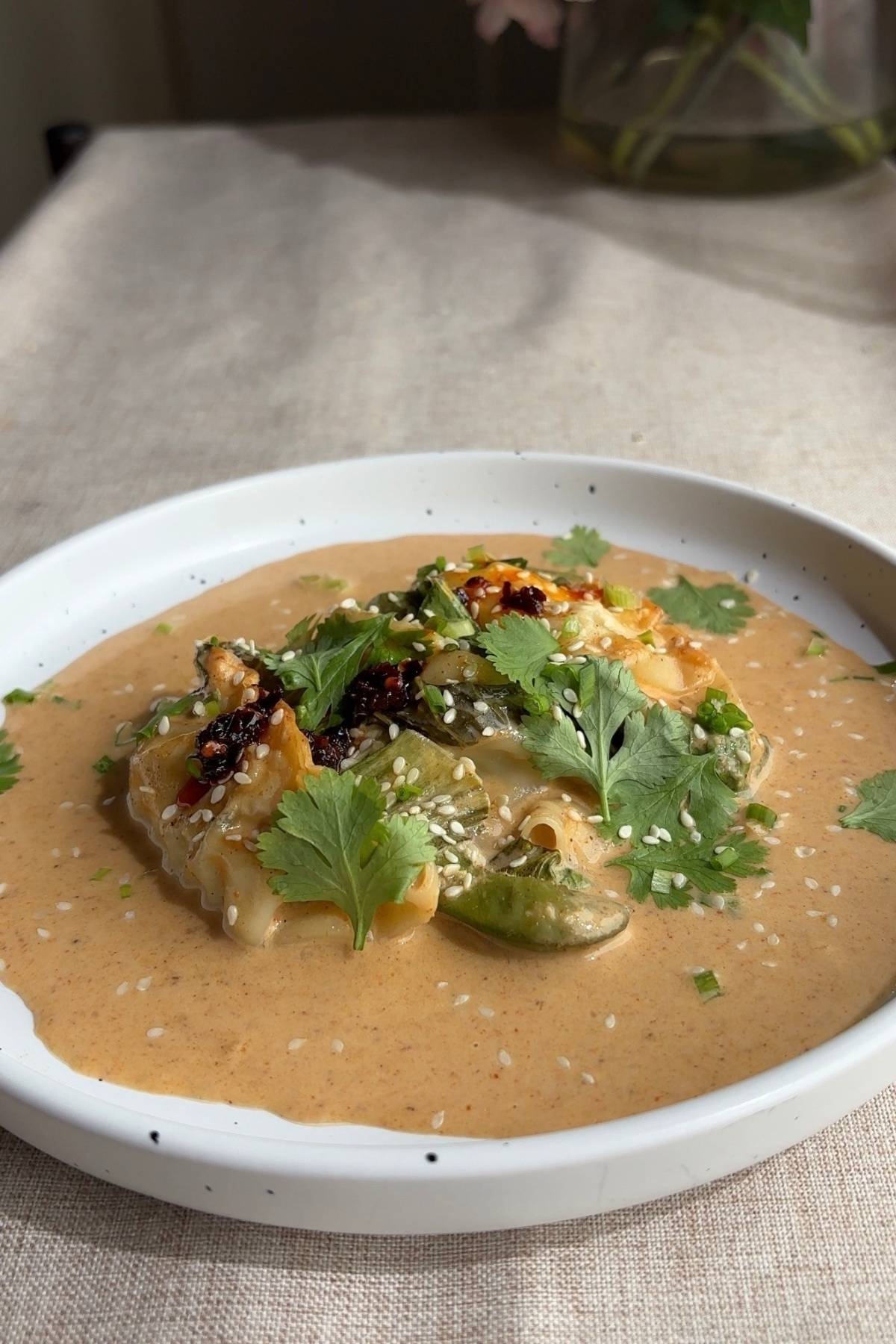 Close-up of baked dumplings resting in thick peanut coconut curry sauce, garnished with fresh coriander, sesame seeds, and chilli oil.