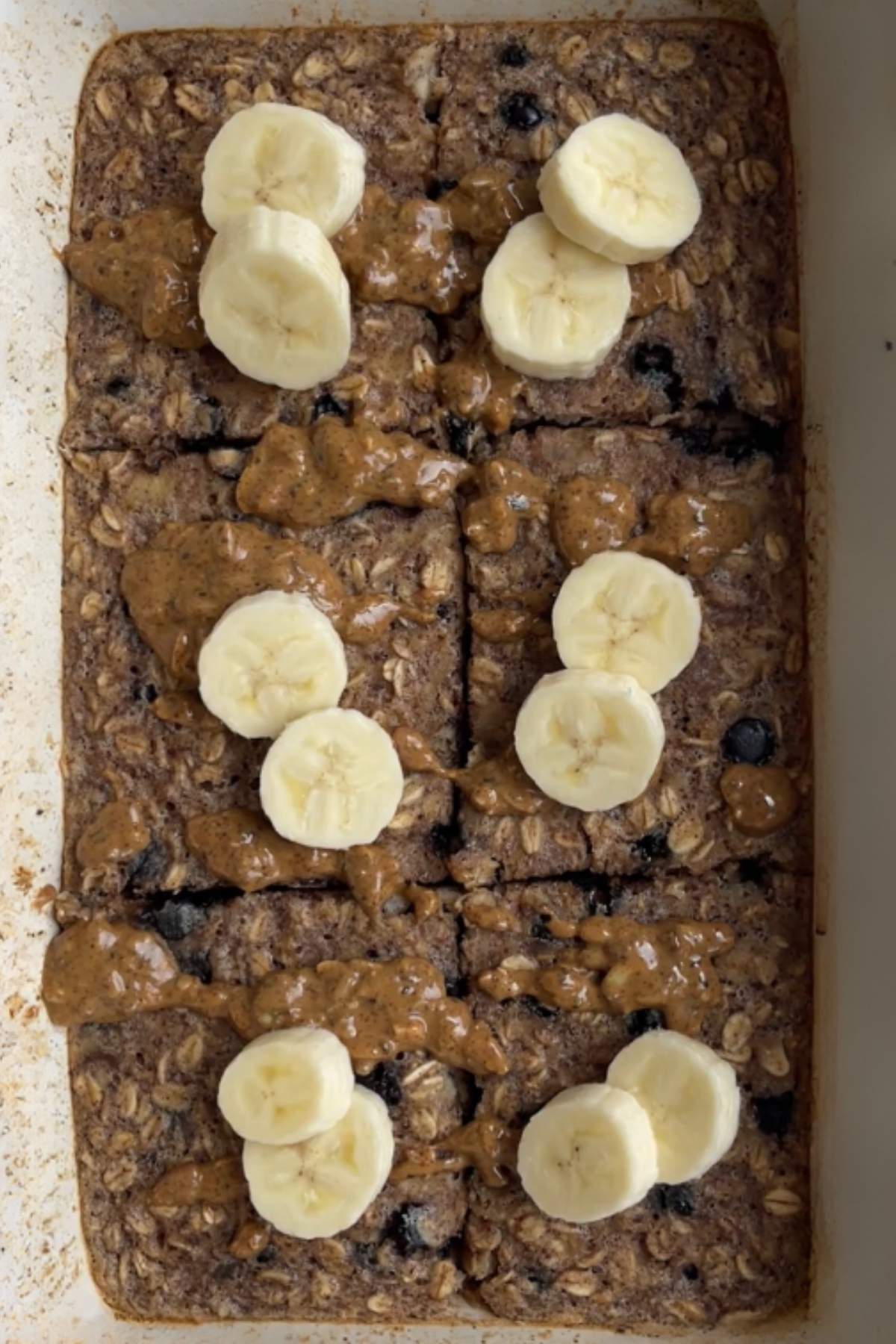 Banana chocolate chip baked oats cut into squares and topped with banana slices and nut butter drizzle.