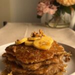 A stack of pancakes topped with banana slices and walnuts.