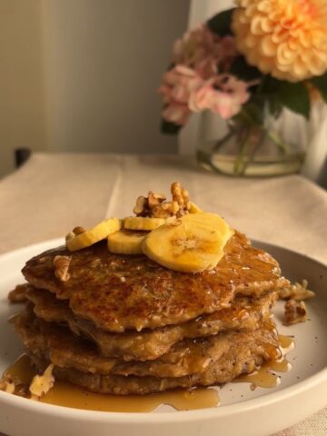 A stack of pancakes topped with banana slices and walnuts.