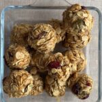 Glass dish filled with oat and cranberry balls sitting on a neutral tablecloth.
