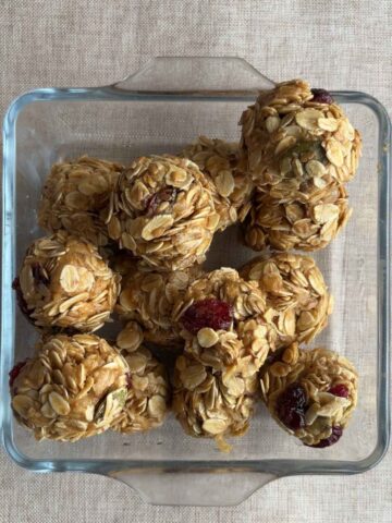 Glass dish filled with oat and cranberry balls sitting on a neutral tablecloth.