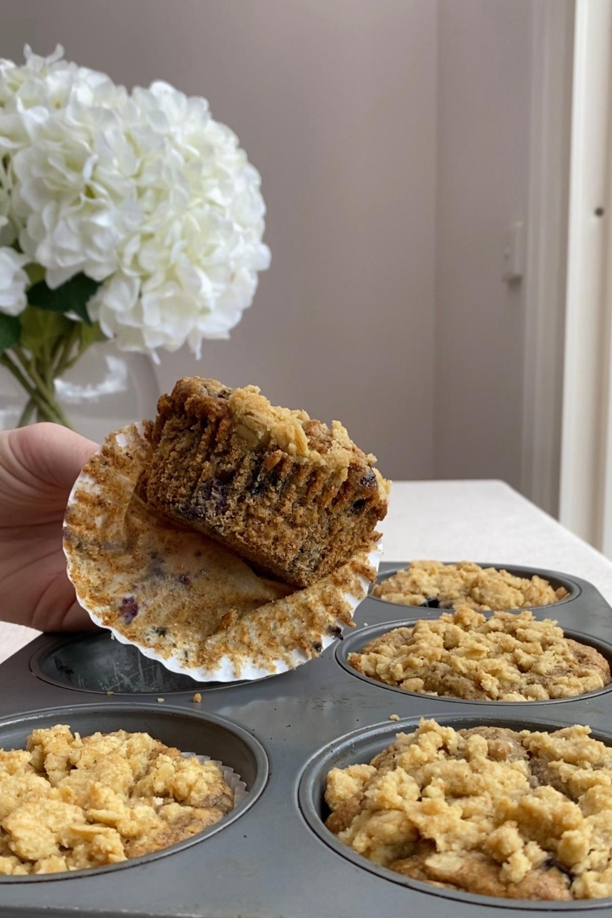 Blueberry breakfast muffin with oat streusel topping held close to the camera, soft interior visible.